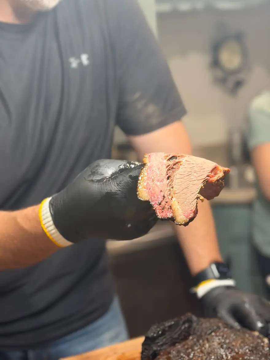 A gloved hand holding up a single slice of brisket