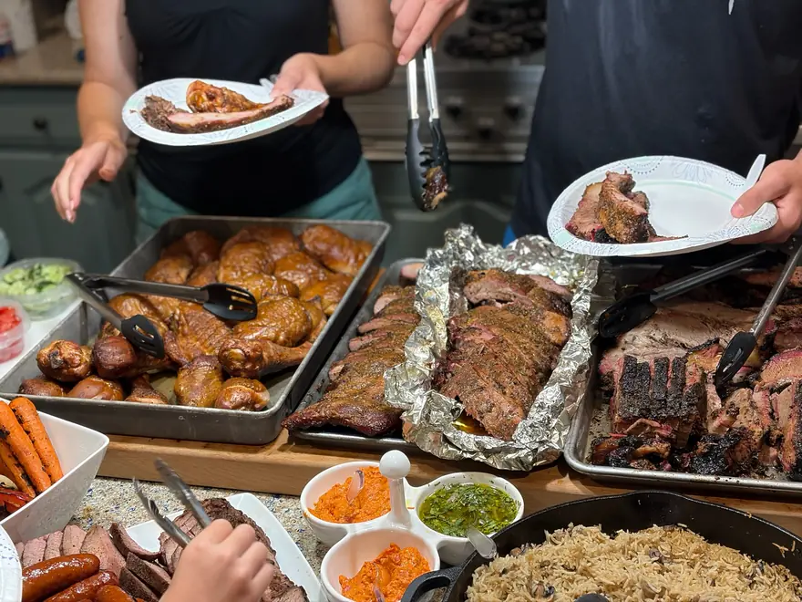 Guests filling plates from a spread of brisket, ribs, chicken and sides
